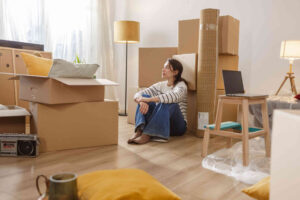 Shot of a young woman packing her belongings in boxes and preparing them for the move. She sits on the floor and thinks